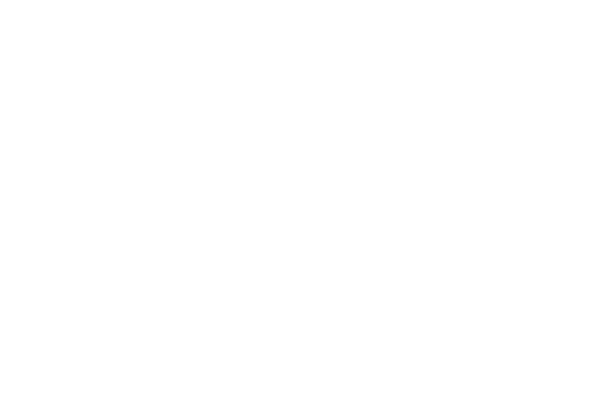 A veteran machinist explaining a part to a younger worker at a bench